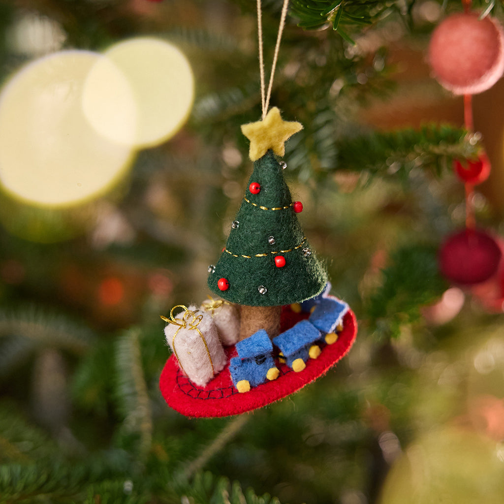 Craftspring’s Train Around the Christmas Tree Ornament displayed on a Christmas tree — felt blue toy train circling the base of a decorated tree with presents, adding festive warmth and whimsical holiday charm — heirloom-quality Christmas decor, ethically crafted by artisans using sustainable wool.