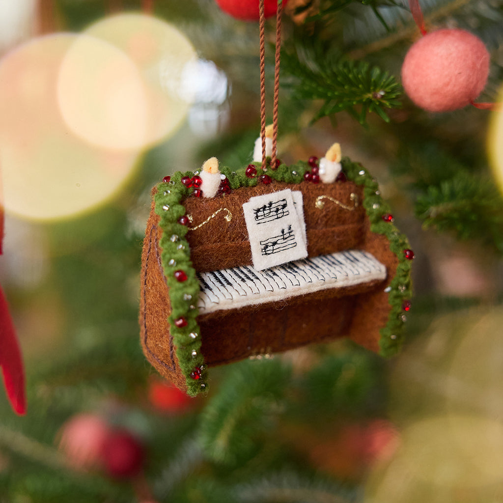Christmas Piano Ornament displayed on a Christmas tree — handmade felt heirloom with embroidered sheet music, beaded details, and festive accents, ethically crafted by artisans using sustainable wool, perfect for holiday gifting.