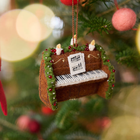 Christmas Piano Ornament displayed on a Christmas tree — handmade felt heirloom with embroidered sheet music, beaded details, and festive accents, ethically crafted by artisans using sustainable wool, perfect for holiday gifting.