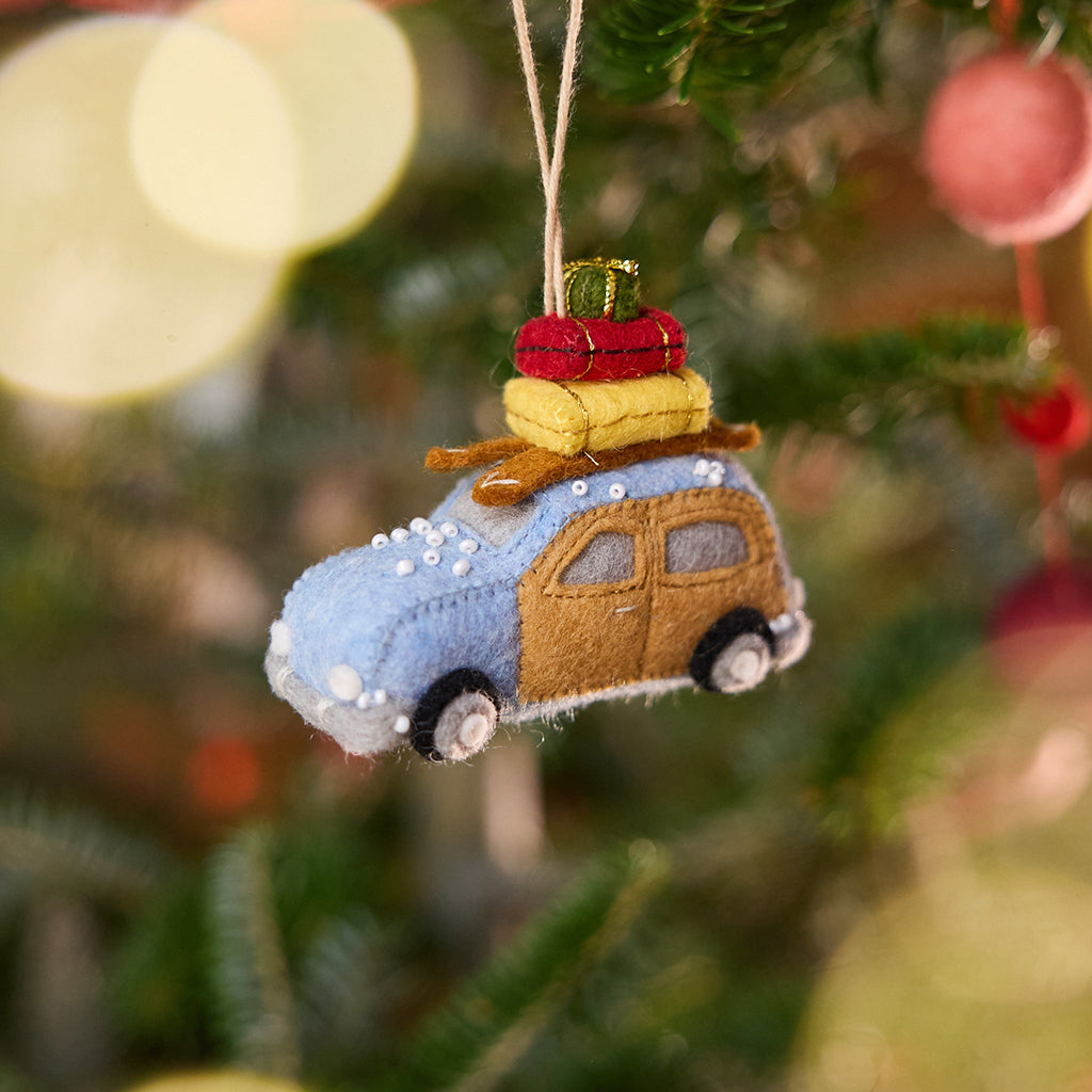 Craftspring’s Station Wagon with Luggage Ornament displayed on a Christmas tree — felt blue station wagon carrying luggage, skis, and presents, adorned with beaded snow, adding festive warmth and playful holiday charm — heirloom-quality Christmas decor, ethically crafted by artisans using sustainable wool.