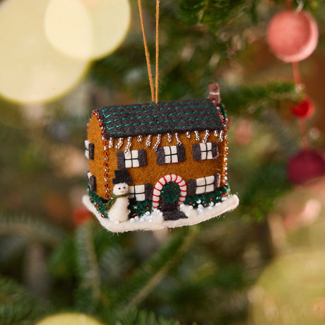 Craftspring’s Christmas House Ornament displayed on a Christmas tree — felt house with detailed beading, embroidery, and applique, featuring a snowman in the yard, beaded icicles on the roof, and holly bushes around the house, adding festive warmth and whimsical holiday charm — heirloom-quality Christmas decor, ethically crafted by artisans using sustainable wool.