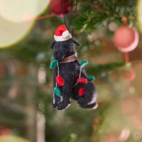 Craftspring’s Black Lab in Christmas Lights Ornament displayed on a Christmas tree — felt dog wrapped in Christmas lights and wearing a Santa hat, adding playful holiday charm and festive warmth — heirloom-quality Christmas decor, ethically crafted by artisans using sustainable wool.