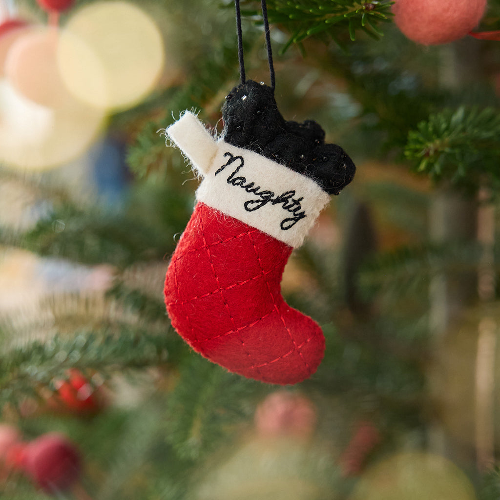 Craftspring’s Naughty Stocking with Coal Ornament displayed on a Christmas tree — felt red stocking filled with felt coal and beads, embroidered “naughty,” adding playful holiday charm and festive warmth — heirloom-quality Christmas decor, ethically crafted by artisans using sustainable wool.