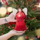 Craftspring’s Praying Angel Tree Topper - Light — felt angel in a red dress with white beads, with embroidered and beaded wreath crown and hands in prayer — held in hand in front of a Christmas tree, capturing cozy holiday magic, whimsical charm, and heirloom-quality gifting, ethically crafted by artisans using sustainable wool.