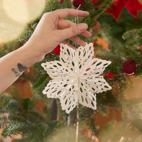 Craftspring’s Paper Snowflakes Christmas Ornaments — Set of 2, smaller white snowflake with intricate cutout patterns, held in front of a Christmas tree, showcasing its delicate design and festive holiday charm, ethically handmade by artisans from recycled cotton waste.
