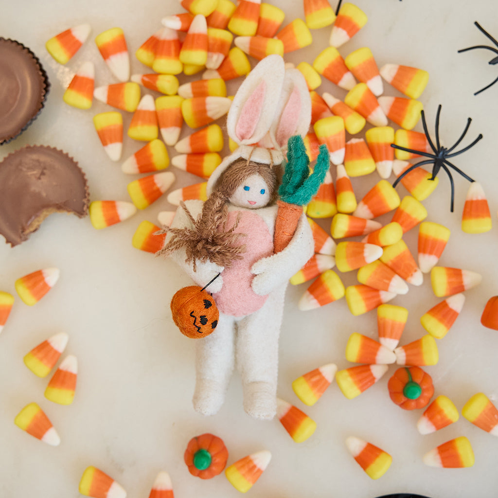 Craftspring’s handmade felt Easter Bunny Trick-Or-Treater ornament — featuring a girl in an Easter Bunny costume holding a pumpkin basket, displayed among candy corn for a festive Halloween scene, perfect for Halloween, autumn, and holiday gifting, ethically crafted by artisans using sustainable wool.