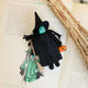 Craftspring’s Wicked Witch Trick-or-Treater ornament — with green skin, a witch’s hat, broom, and pumpkin basket — displayed on the book Wicked for a festive Halloween scene, perfect for spooky decorating and holiday gifting, ethically crafted by artisans using sustainable wool.