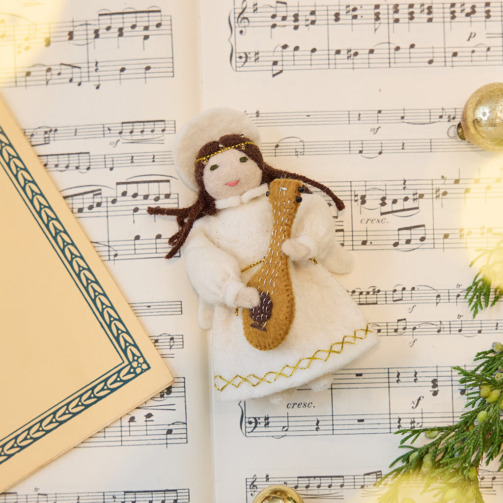 Vintage-Style Angel Playing Lute Ornament displayed on sheet music — handmade felt holiday ornament with beaded and golden embroidered details, showing an angel playing a lute, ethically crafted by artisans using sustainable wool.