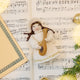 Vintage-Style Angel Playing Lute Ornament displayed on sheet music — handmade felt holiday ornament with beaded and golden embroidered details, showing an angel playing a lute, ethically crafted by artisans using sustainable wool.