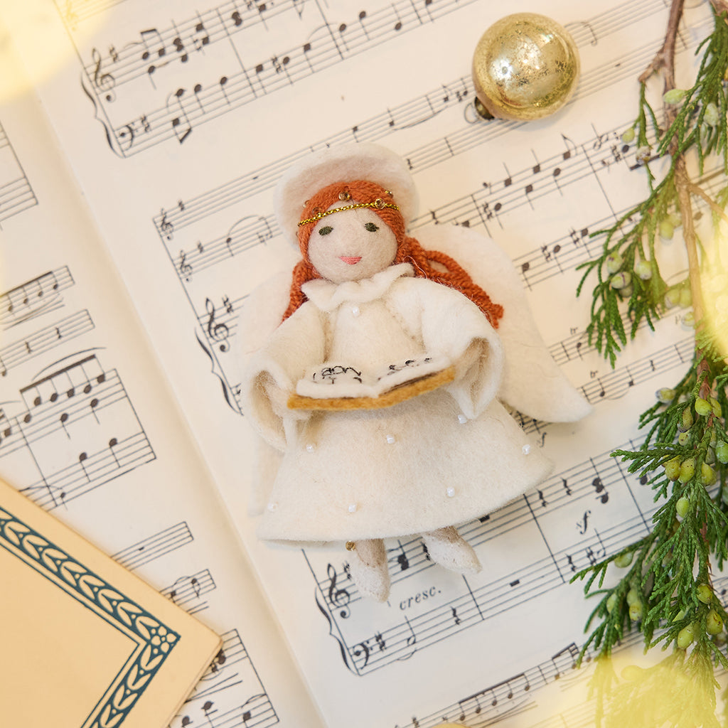 Vintage-Style Angel Singing Noel Ornament displayed on sheet music — handmade felt holiday ornament with intricate beaded and embroidered details, showing an angel singing Noel, ethically crafted by artisans using sustainable wool.