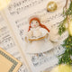 Vintage-Style Angel Singing Noel Ornament displayed on sheet music — handmade felt holiday ornament with intricate beaded and embroidered details, showing an angel singing Noel, ethically crafted by artisans using sustainable wool.