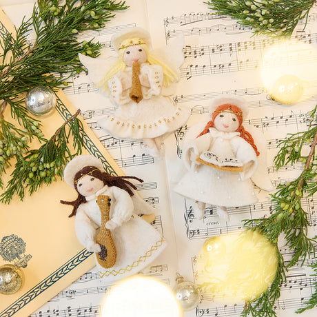 Craftspring’s Vintage-Style Angel Playing Lute, Vintage-Style Angel Playing Trumpet, and Vintage-Style Angel Singing Noel ornaments displayed together on sheet music — handmade felt holiday ornaments with sweet faces, intricate beaded and embroidered details, ethically crafted by artisans using sustainable wool for festive Christmas gifting.