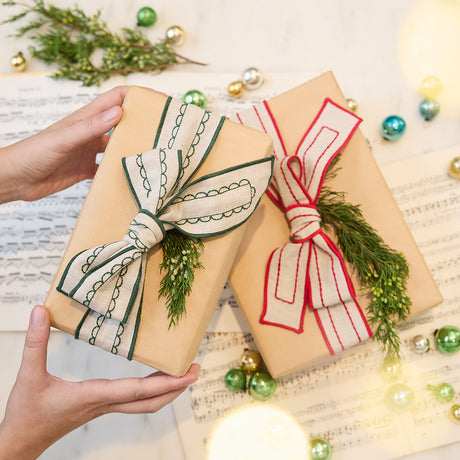Craftspring’s Embroidered Linen Ribbons tied around Christmas presents, with one gift held in hand — featuring red and green embroidery on natural linen for a festive and thoughtful holiday detail, ethically crafted by artisans.