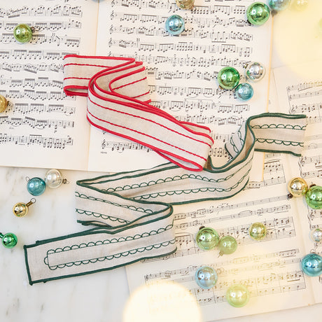 Craftspring’s Embroidered Linen Ribbons — one red, one green — displayed on sheet music with evergreens for a timeless Christmas scene, handmade on natural linen and ethically crafted by artisans.