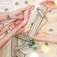 Craftspring’s Embroidered Linen Ribbons set — one with red embroidery, one with green — held in hand over sheet music with evergreens, highlighting their festive handmade details, ethically crafted by artisans.