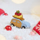 Craftspring’s Station Wagon with Luggage Ornament — felt blue station wagon carrying suitcases, skis, and presents on top, with beaded snow details — displayed on snow among holiday baubles and peppermints, evoking playful Christmas cheer, festive warmth, and heirloom-quality gifting, ethically crafted by artisans using sustainable wool.