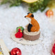 Craftspring’s Fox on Stump ornament — a fox perched on a stump with a green present and red cardinal — displayed on snow with bobbles and evergreens for a cozy woodland Christmas scene, perfect for holiday gifting, ethically crafted by artisans using sustainable wool.