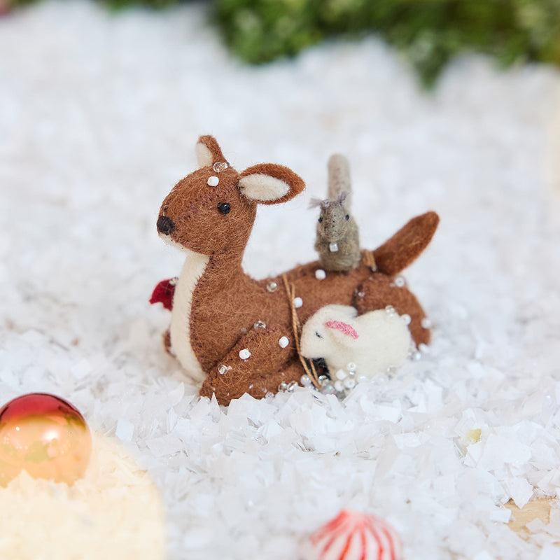 Craftspring’s Sitting Deer with Friends ornament — featuring a deer in the snow with a bunny, squirrel, and bird nestled around it, with intricate beaded snow and embroidered details — displayed in the snow with bobbles for a festive Christmas scene, ethically crafted by artisans using sustainable wool.