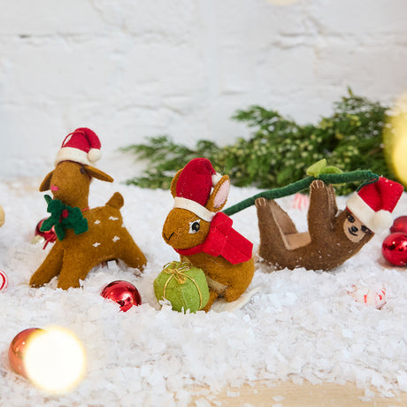 Craftspring’s Santa Animals Ornaments Bundle — includes Santa Fawn Ornament, Brown Santa Bunny Ornament, and Lazy Santa Sloth Ornament — displayed together in a cozy holiday setting, highlighting playful designs with Santa hats and sweet holiday details, evoking festive warmth and heirloom-quality Christmas gifting, ethically crafted by artisans using sustainable wool.