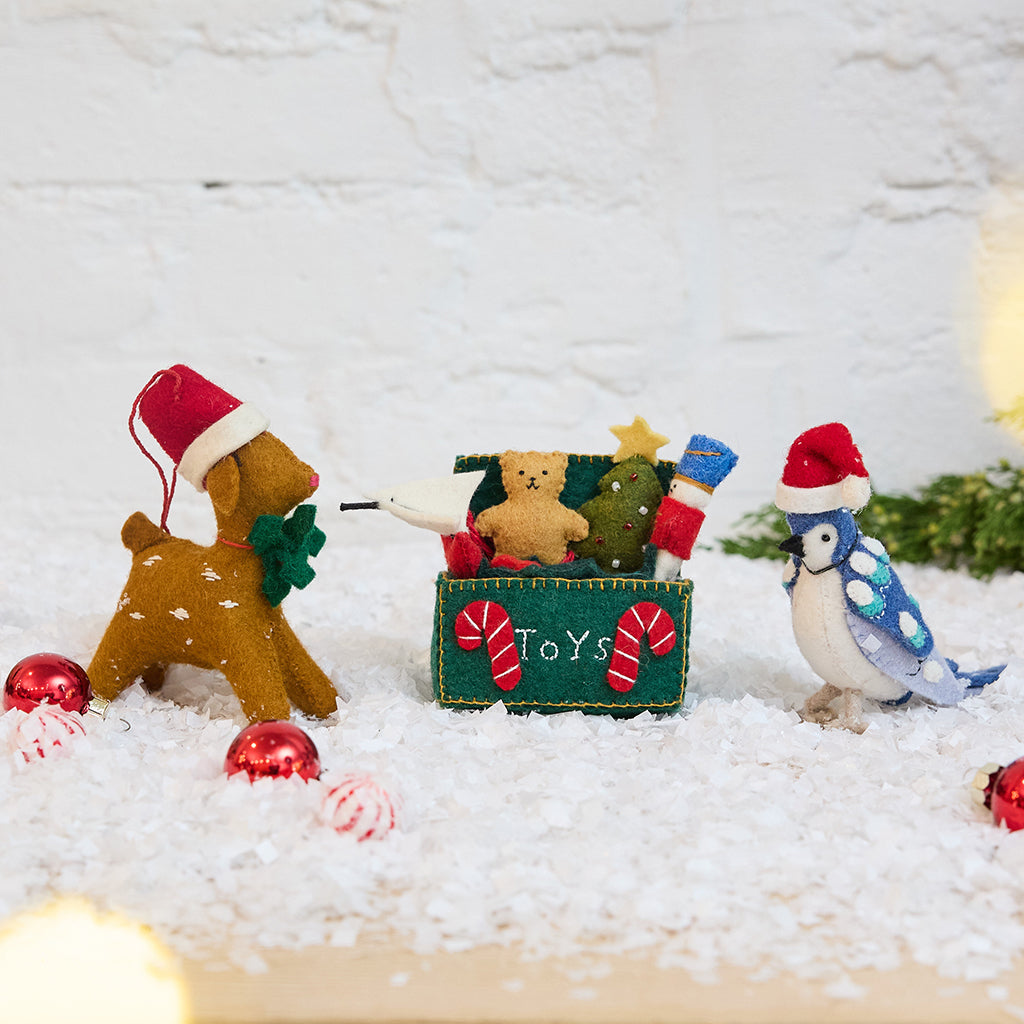 Craftspring’s Santa’s Favorites Ornaments Bundle — includes Santa Fawn Ornament, Santa Blue Jay Ornament, and Toy Box Ornament — displayed together in a cozy holiday setting, highlighting playful designs with beaded and embroidered details, two animals wearing Santa hats, and a toy-filled box, evoking festive warmth and heirloom-quality Christmas gifting, ethically crafted by artisans using sustainable wool.