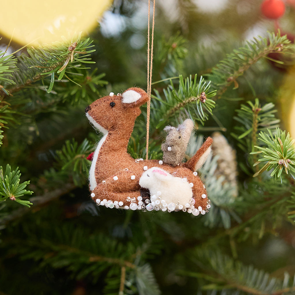 Craftspring’s Sitting Deer with Friends ornament — featuring a deer with a bunny, squirrel, and bird nestled around it, with intricate beaded snow and embroidered details — displayed on a Christmas tree for a festive woodland holiday scene, ethically crafted by artisans using sustainable wool.