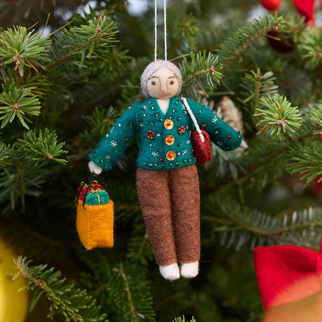 Handmade felt Grandma ornament from Craftspring, wearing a cozy beaded and embroidered holiday sweater, holding a designer purse and a shopping bag full of presents—displayed on a Christmas tree, evoking warm holiday memories and timeless festive cheer, ethically crafted by artisans using sustainable wool.