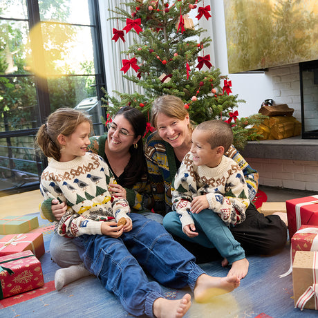 Craftspring’s NYC Holiday 100% Alpaca Sweater Cardigan — heirloom-quality cardigan knit from ultra-soft baby alpaca wool, sustainably harvested and adorned with jacquard motifs of NYC icons like bagels, pigeons, and taxi cabs — ethically made by artisans in Peru. A family wears the cardigans together in front of a Christmas tree, celebrating festive cheer, heirloom holiday style, and the joy of Christmas gifting.