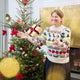 Craftspring’s NYC Holiday 100% Alpaca Sweater — heirloom-quality crewneck crafted of ultra-soft, sustainably harvested baby alpaca wool with intricate jacquard NYC motifs such as bagels, pigeons, and taxi cabs — ethically made by artisans in Peru. A woman wears the sweater in front of a Christmas tree, radiating Christmas elegance, warmth, and holiday gifting joy.