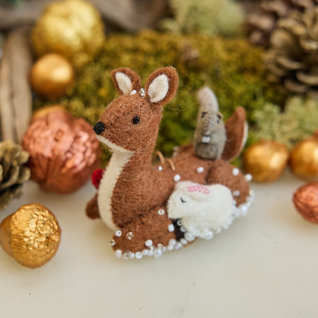 Handmade felt Sitting Deer with Friends Ornament from Craftspring, featuring a deer, rabbit, squirrel, and bird surrounded by beaded snow—displayed in a festive woodland holiday scene with golden walnuts and moss, perfect for Christmas gifting, ethically crafted by artisans using sustainable wool.