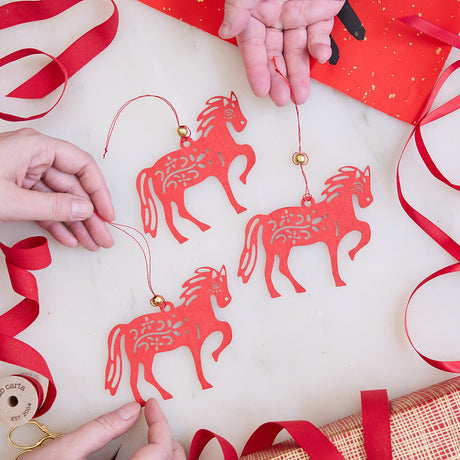 Paper Lantern Ornaments held in hand among loops of red ribbon, glowing with delicate cutout designs. Ethically handmade by artisans for Lunar New Year gifting and timeless decor.