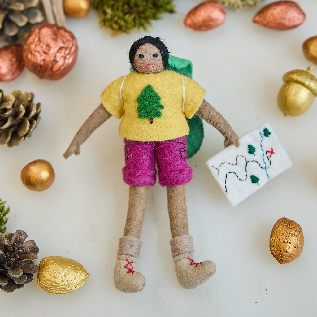 Handmade felt On the Trail Backpacker Ornament – Brown from Craftspring, backpacker girl with map and colorful hiking clothes—displayed among golden nuts in a festive holiday scene, heirloom-quality Christmas decor, ethically handcrafted by artisans.