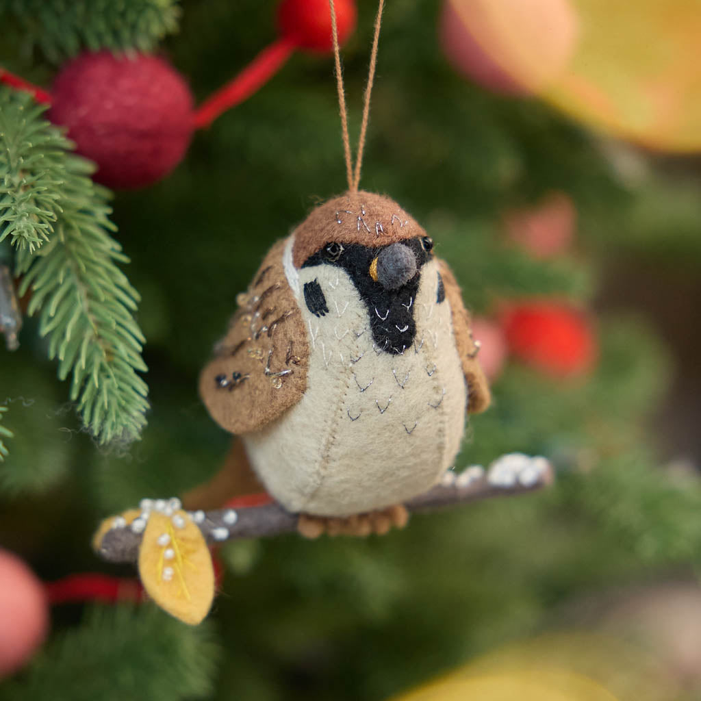 Celebrate the quiet beauty of everyday birds with our Sparrow Ornament. Small yet full of personality, this beloved garden bird is lovingly hand-felted from natural wool and perched on a delicate felt branch.