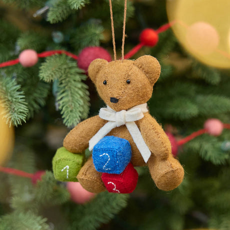 Classic and comforting, this adorable teddy bear ornament is crafted from soft, natural wool felt and finished with a gentle cream scarf. Nestled beside colorful number blocks, it captures the sweetness of early childhood and the joy of new beginnings.