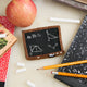 Miniature chalkboard with educational drawings, pencils, and an apple on a light surface. 
A double-sided handmade felt school blackboard ornament featuring a world map on one side and classic math formulas on the other. An ode to old-school learning and the teachers that inspired us.