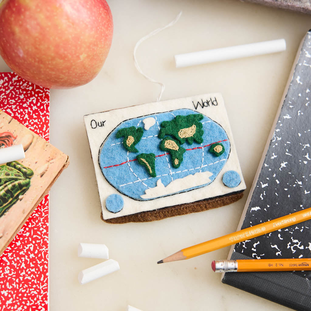 Small world map model ornament on a desk with an apple, notebook, and pencils.