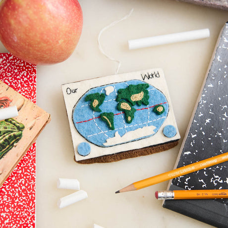 Small world map model ornament on a desk with an apple, notebook, and pencils.