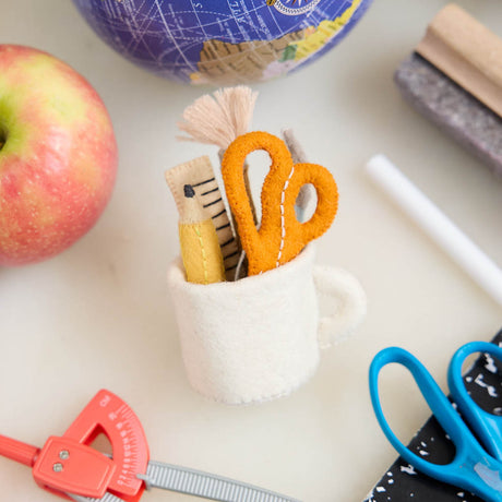 Bring the charm of the classroom and the drafting table to your holiday décor with our&nbsp;Pencil Cup Felt Ornament. This handcrafted design features a soft wool felt mug filled with iconic school and creative essentials—bright scissors, a pencil, a paintbrush, a fountain pen, and a ruler—capturing the everyday magic of learning and creativity.&nbsp;
