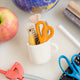 Bring the charm of the classroom and the drafting table to your holiday décor with our&nbsp;Pencil Cup Felt Ornament. This handcrafted design features a soft wool felt mug filled with iconic school and creative essentials—bright scissors, a pencil, a paintbrush, a fountain pen, and a ruler—capturing the everyday magic of learning and creativity.&nbsp;