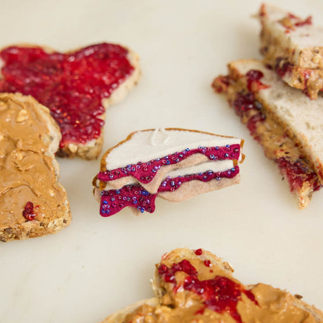 Bread slices with peanut butter and jelly on a white surface This handcrafted design captures the classic peanut butter and jelly sandwich, complete with layered bread and vibrant jelly details; Go back in time with this classic sandwich ornament - think cafeteria lunches, hallway memories, dad packing your brown-paper bag lunch. This is a time-capsule!