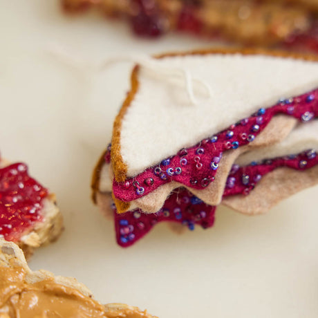 Bring a touch of lunchtime nostalgia to your holiday décor with our PB &amp; J Felt Ornament. This handcrafted design captures the classic peanut butter and jelly sandwich, complete with layered bread and vibrant jelly details.&nbsp; Go back in time with this classic sandwich ornament - think cafeteria lunches, hallway memories, dad packing your brown-paper bag lunch. This is a time-capsule!