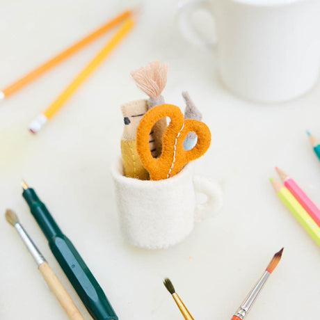 Bring the charm of the classroom and the drafting table to your holiday décor with our&nbsp;Pencil Cup Felt Ornament. This handcrafted design features a soft wool felt mug filled with iconic school and creative essentials—bright scissors, a pencil, a paintbrush, a fountain pen, and a ruler—capturing the everyday magic of learning and creativity.&nbsp;
