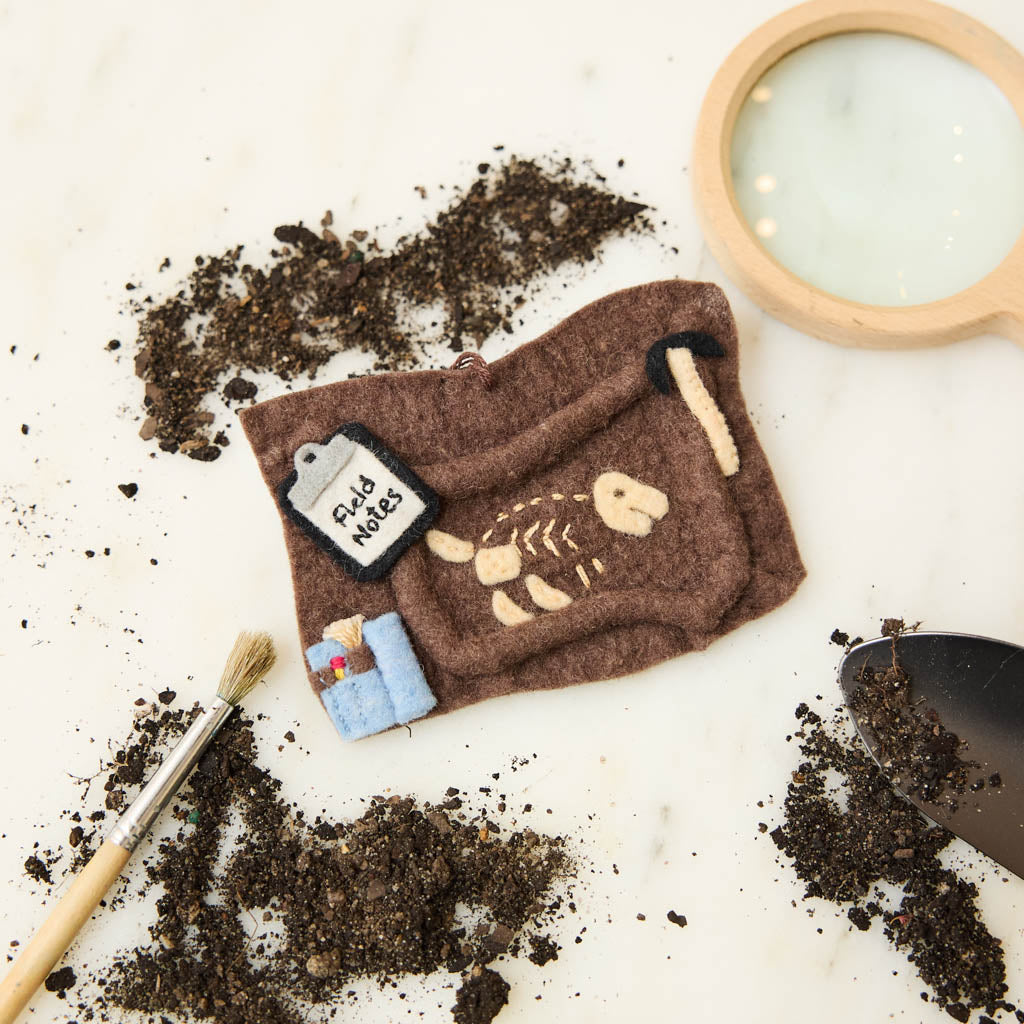 Unearth a piece of prehistoric wonder with our Felt Dinosaur Bones Ornament. Carefully handcrafted by skilled artisans using sustainable wool felt, this charming ornament features an excavation scene complete with partially uncovered dinosaur fossils, excavation tools, field notes, and scientific equipment.