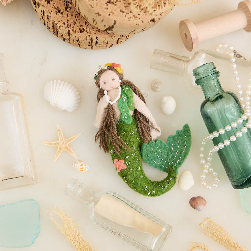 Add a touch of ocean magic to your Christmas tree with our beautiful Siren Mermaid Ornament. Lovingly handcrafted from eco-friendly wool felt, this elegant mermaid features flowing brunette hair, a vibrant green tail adorned with sparkling bead accents, and charming floral details inspired by the treasures of the sea.
