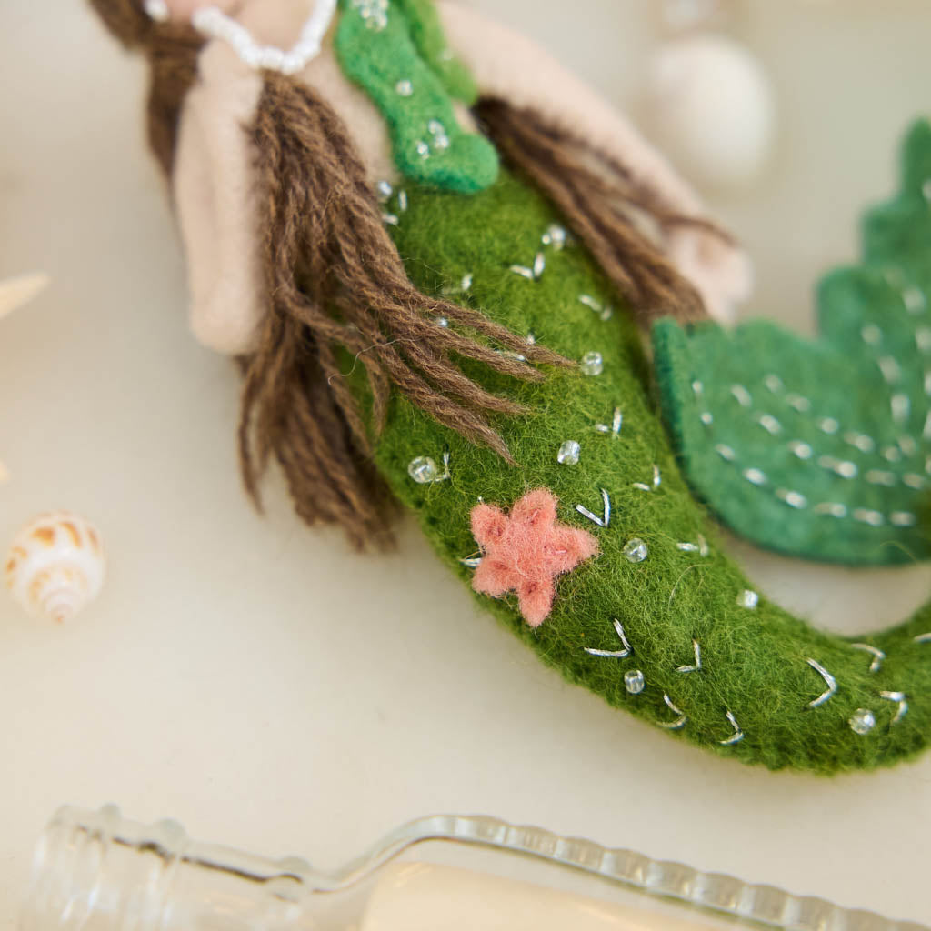 Add a touch of ocean magic to your Christmas tree with our beautiful Siren Mermaid Ornament. Lovingly handcrafted from eco-friendly wool felt, this elegant mermaid features flowing brunette hair, a vibrant green tail adorned with sparkling bead accents, and charming floral details inspired by the treasures of the sea.