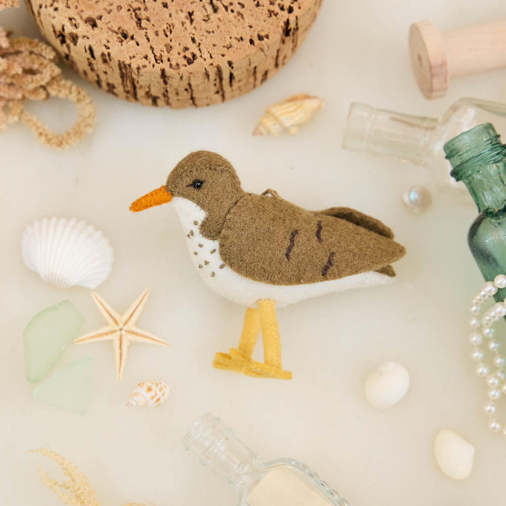Bring a touch of the shoreline to your holiday décor with our delightful Spotted Sandpiper Ornament. Carefully handcrafted from eco-friendly wool felt, this charming bird captures the distinctive features of the beloved sandpiper, from its warm brown plumage and bright orange beak to its delicate spotted breast.