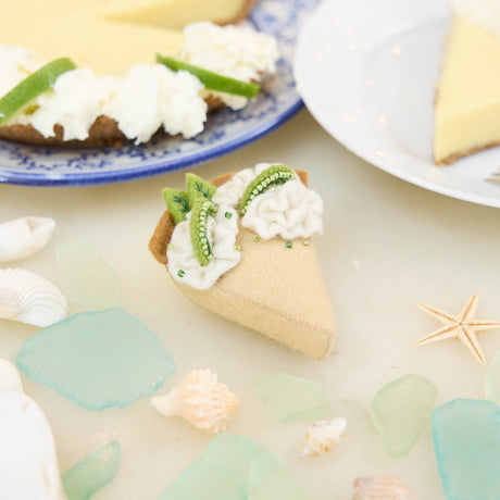 Capture the sweet taste of the Florida Keys with our handcrafted Key Lime Pie Slice Felt Ornament, a delightful dessert-inspired decoration featuring fluffy whipped cream, vibrant lime accents, and realistic pie slice details. Handmade from sustainable wool felt by women artisans, this whimsical ornament celebrates one of America's most beloved tropical desserts and adds a playful touch to holiday décor.