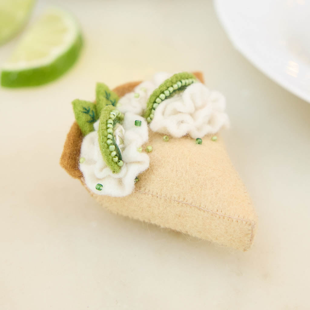 Capture the sweet taste of the Florida Keys with our handcrafted Key Lime Pie Slice Felt Ornament, a delightful dessert-inspired decoration featuring fluffy whipped cream, vibrant lime accents, and realistic pie slice details. Handmade from sustainable wool felt by women artisans, this whimsical ornament celebrates one of America's most beloved tropical desserts and adds a playful touch to holiday décor.