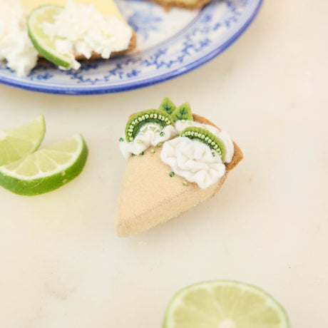 Capture the sweet taste of the Florida Keys with our handcrafted Key Lime Pie Slice Felt Ornament, a delightful dessert-inspired decoration featuring fluffy whipped cream, vibrant lime accents, and realistic pie slice details. Handmade from sustainable wool felt by women artisans, this whimsical ornament celebrates one of America's most beloved tropical desserts and adds a playful touch to holiday décor.
