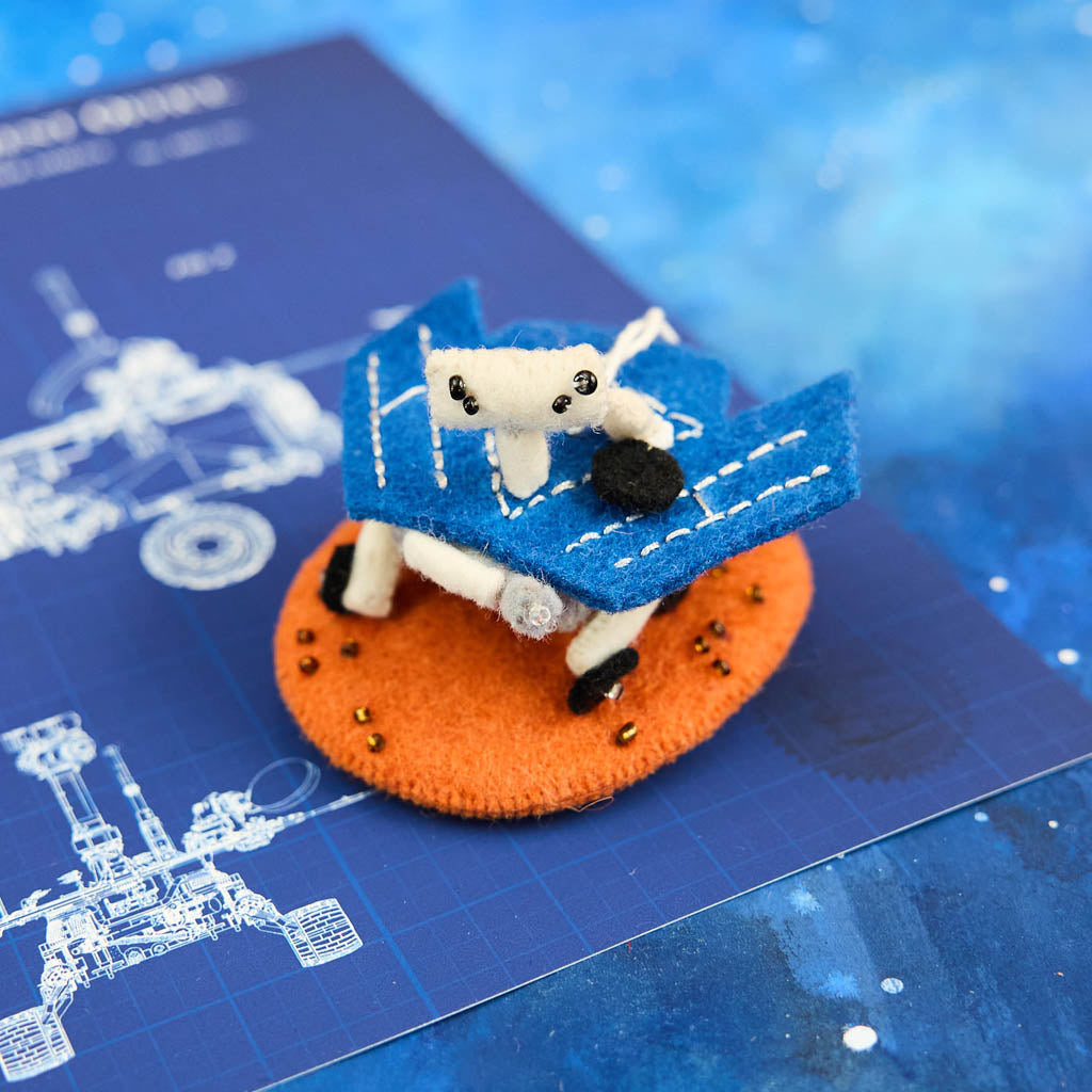 Explore the Red Planet with our handcrafted Mars Opportunity Rover Ornament, inspired by NASA’s legendary Mars Exploration Rover, affectionately known as "Oppy." Designed in soft wool felt with intricate handcrafted details, this ornament captures the iconic rover as it traverses the dusty Martian landscape in search of scientific discoveries.