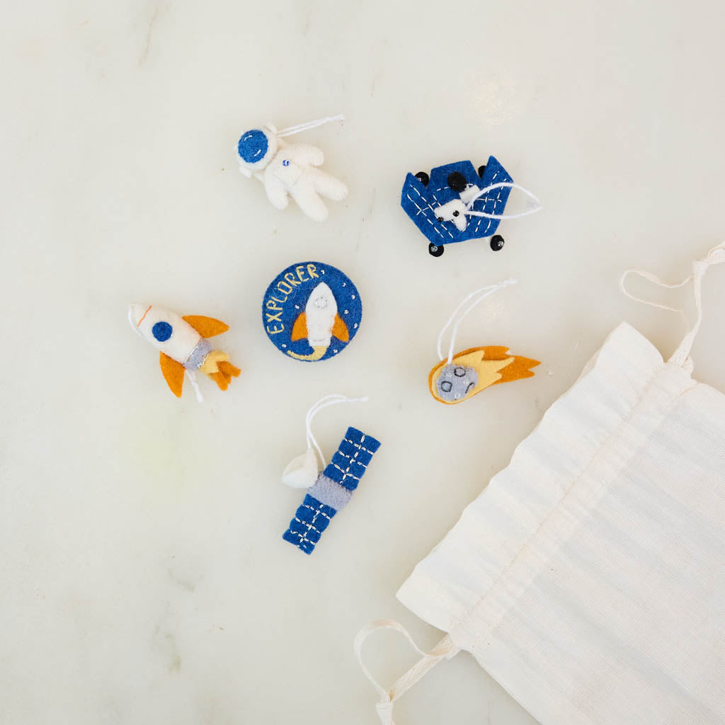 Blast off into a universe of discovery with our Space Mini Ornaments Set. This delightful collection includes five handcrafted felt ornaments inspired by the wonders of space: an astronaut, satellite, space shuttle, rocket ship, and meteor, along with a coordinating Explorer badge that can be displayed as a keepsake or worn as a symbol of curiosity and adventure.